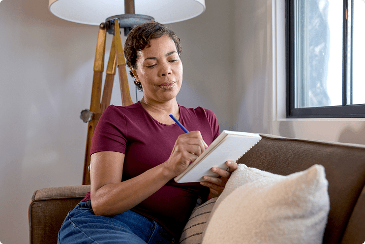 Woman sitting on her couch writing on a pad of paper