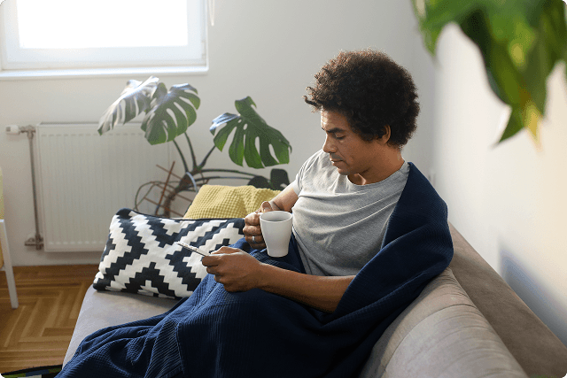 Person sitting on couch drinking coffee and scrolling on phone