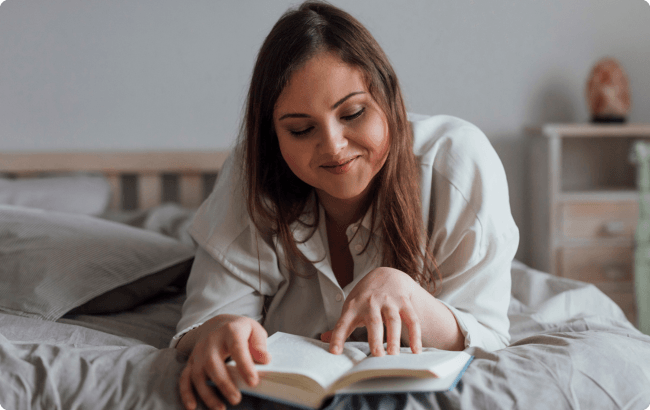 Woman lying on her bed reading a book
