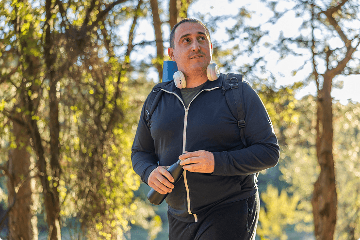 Man walking outside wearing headphones around his neck and carrying a water bottle