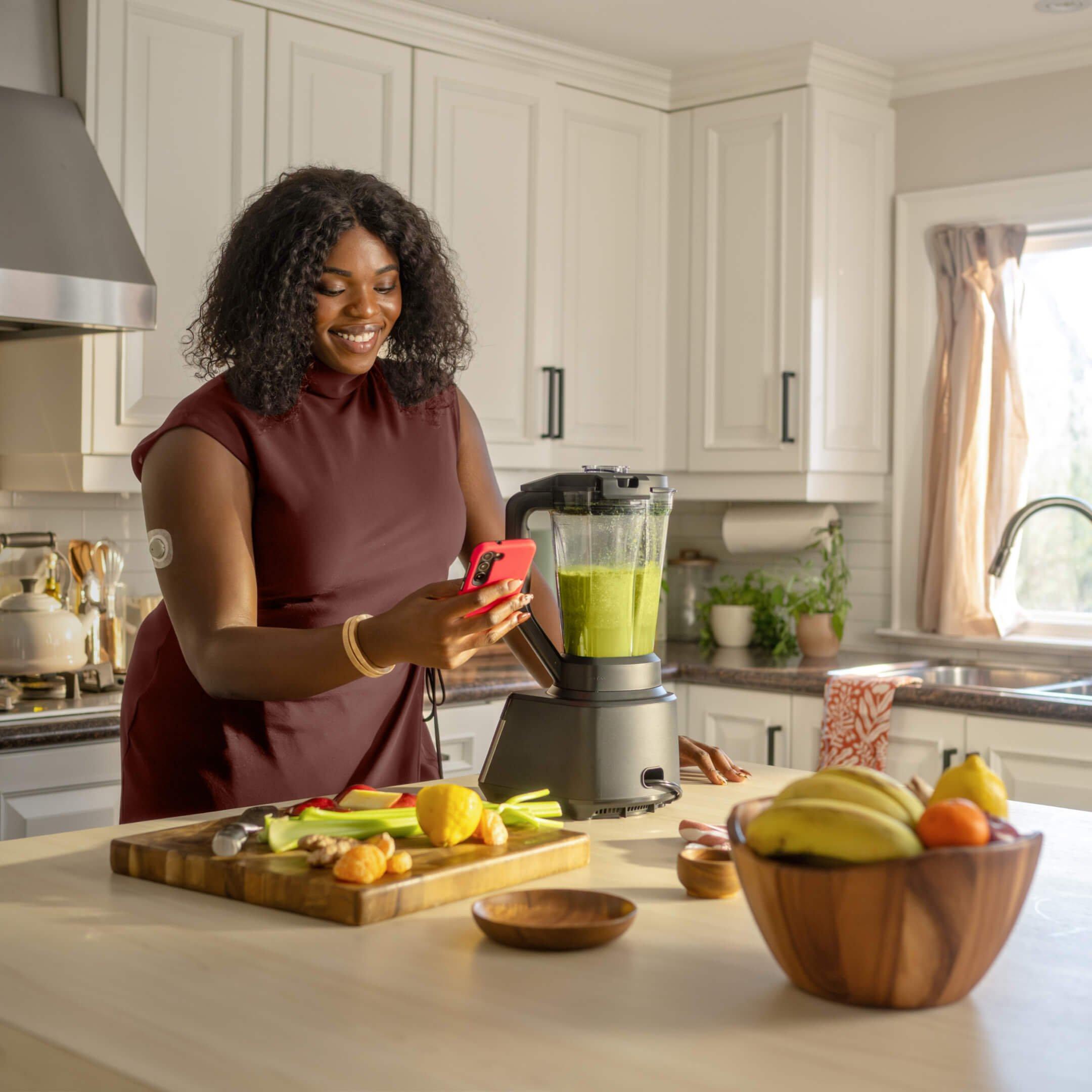 person looking at stelo app on smart device while making a smoothie