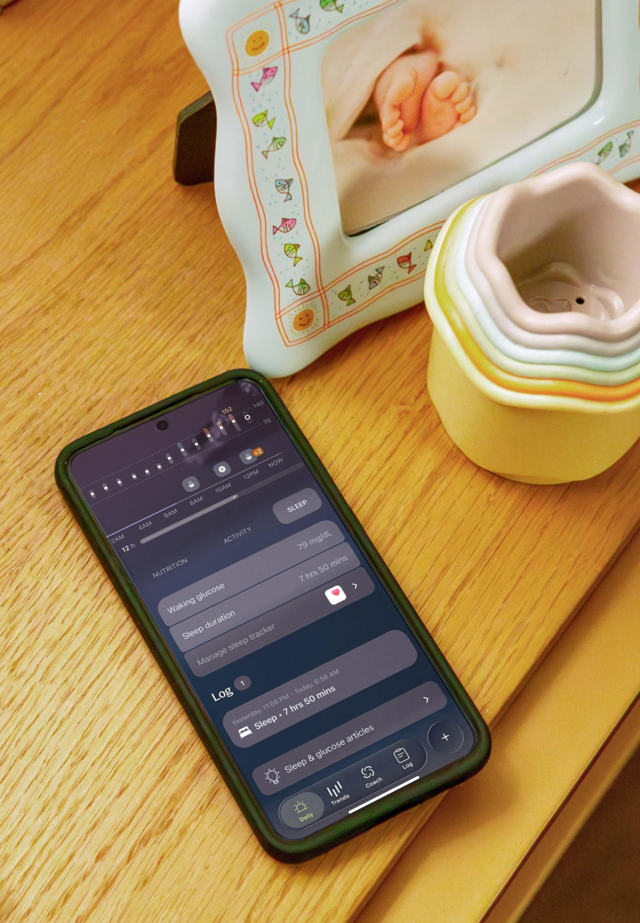 Phone on a table next to a baby photo, showing Stelo app