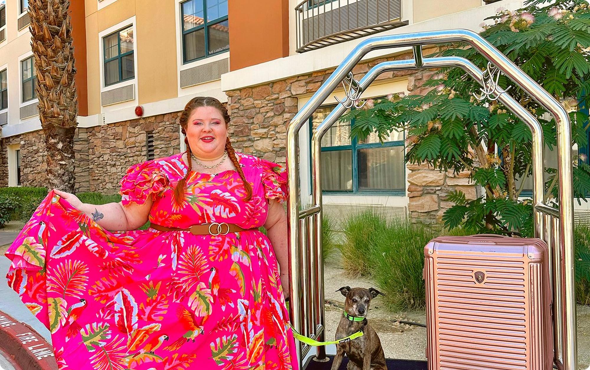 Victoria standing outside in a pink dress with her dog and suitcase