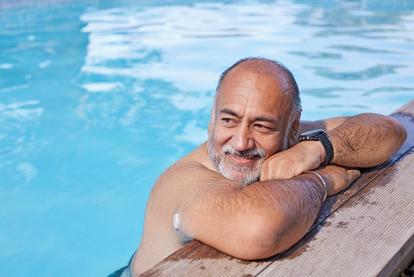 Hombre mayor apoyado en el borde de una piscina con el sensor Dexcom ONE+ en la parte superior del brazo.