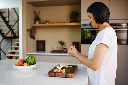 Mujer con sensor Dexcom ONE+ en la parte superior del brazo cortando fruta en una cocina