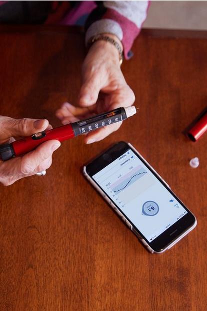 Une personne utilisant un stylo à insuline pour prendre des décisions concernant le traitement du diabète sur la base des données de glycémie de l'application Dexcom G6.