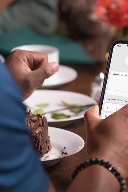 Ein Mann schaut beim Abendessen in seine Dexcom G7-App