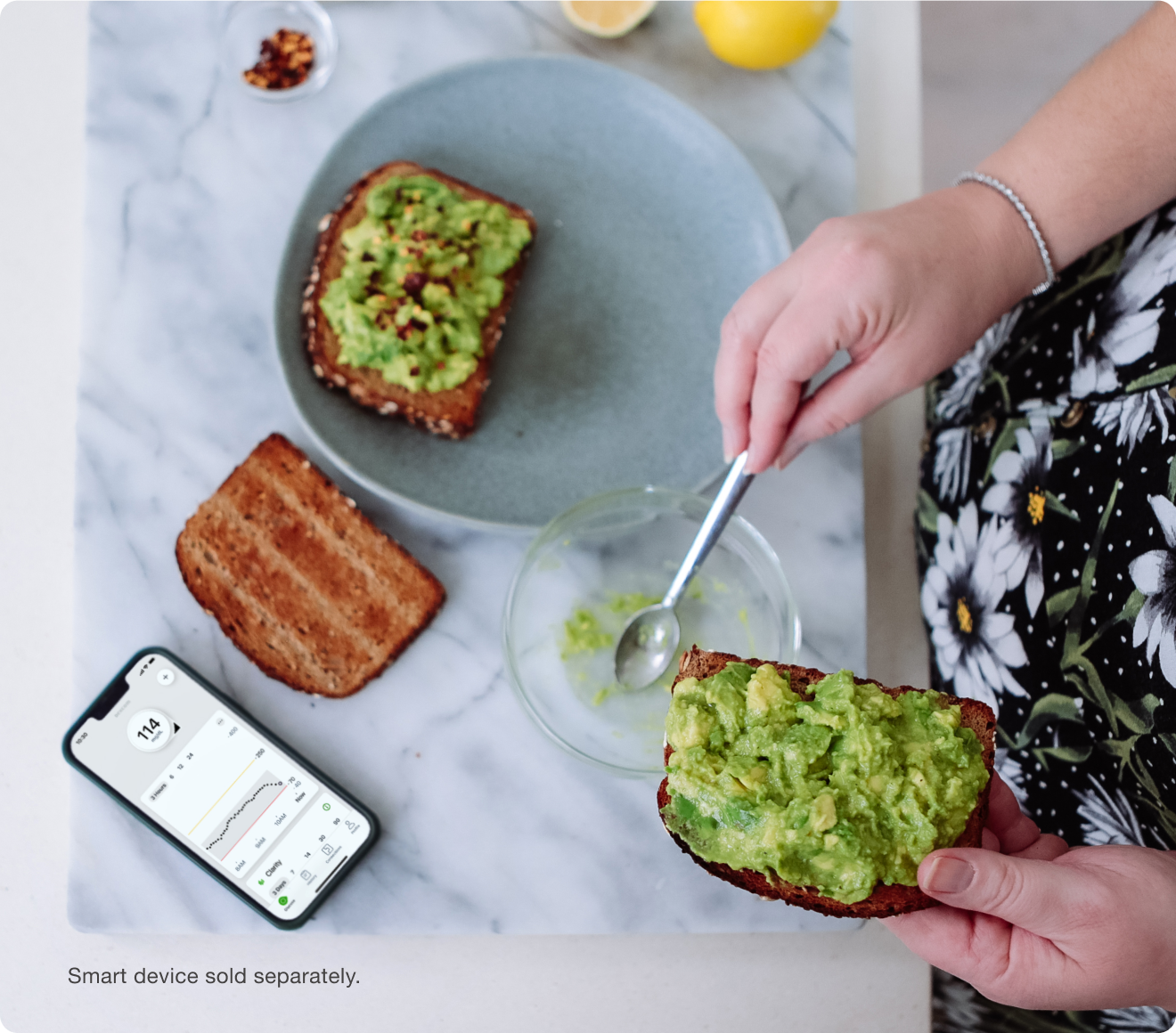 hands putting avocado on toast, phone screen showing glucose numbers - smart devices sold separately