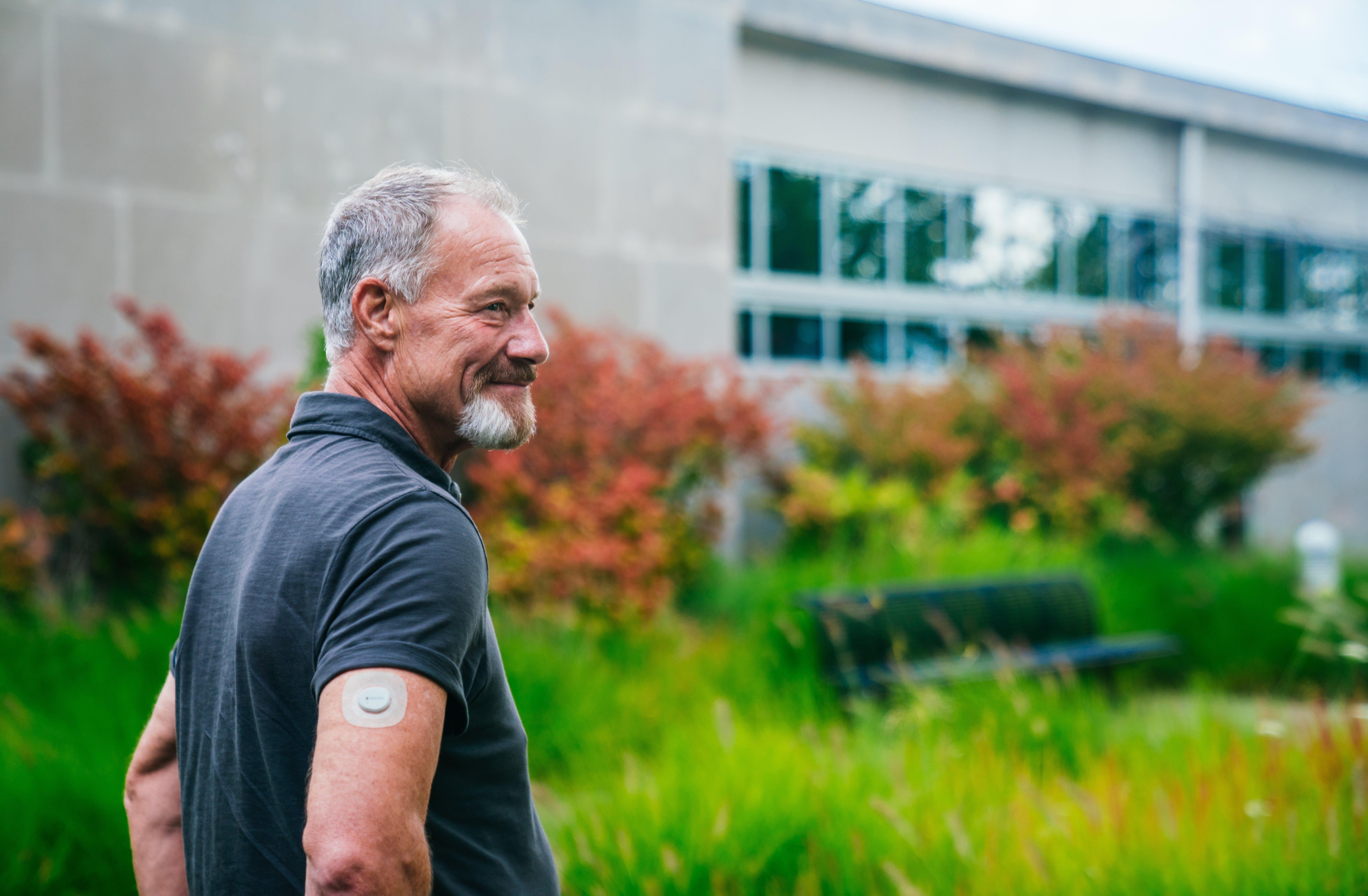 man smiling outdoors wearing dexcom sensor on arm