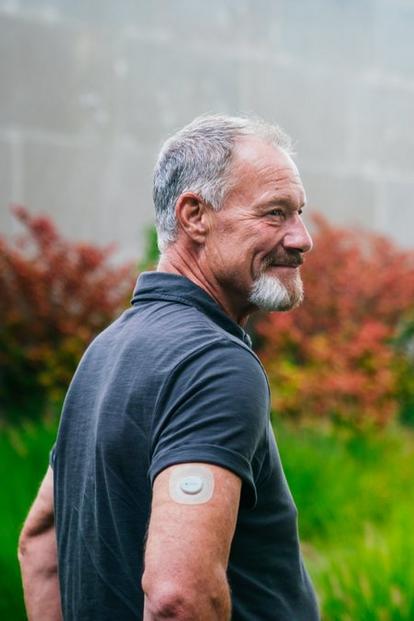 man smiling outdoors wearing dexcom sensor on arm