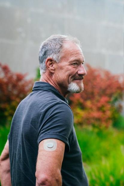 man smiling outdoors wearing dexcom sensor on arm