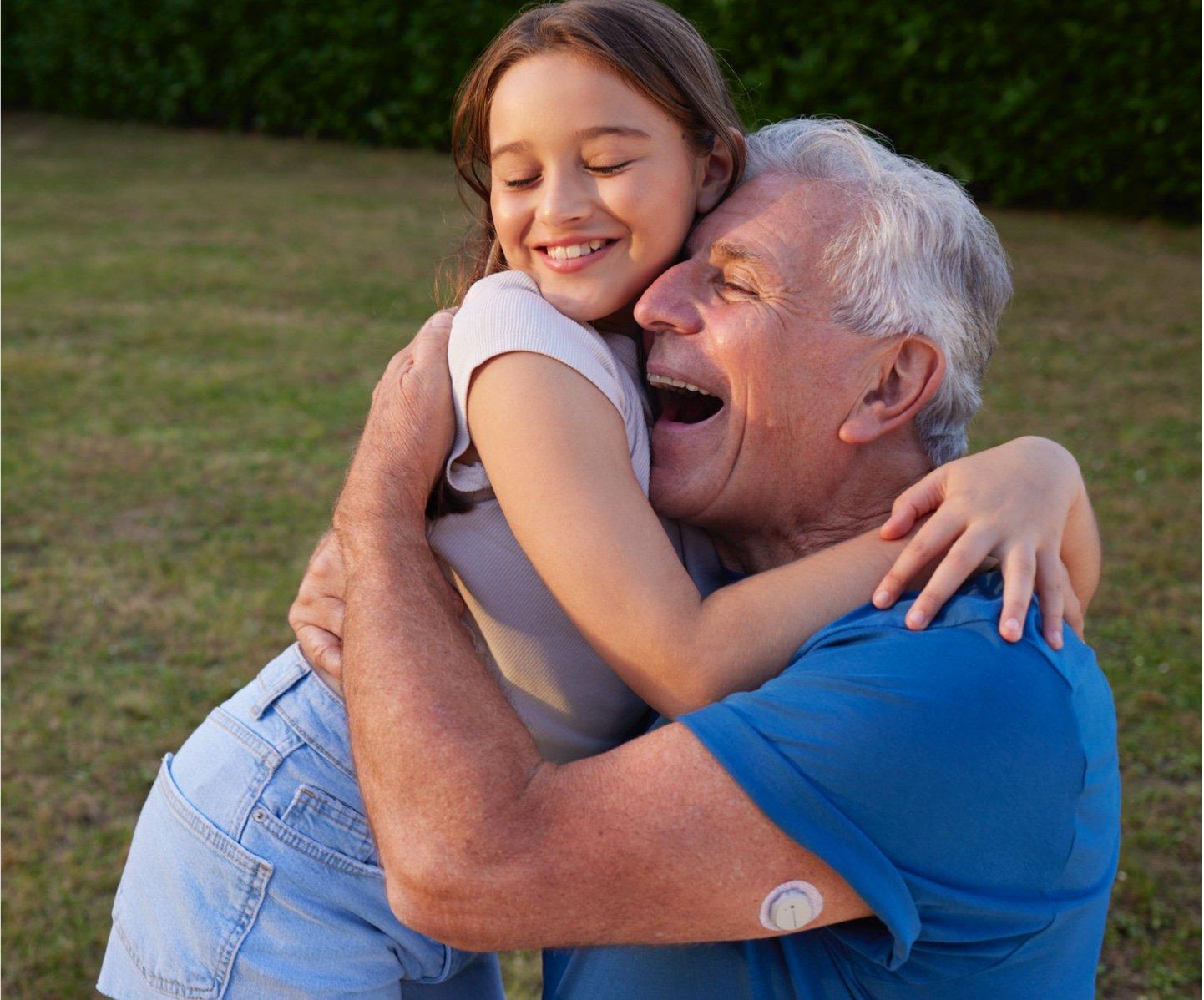 Jong meisje omhelst oudere man met een Dexcom ONE+ sensor op zijn bovenarm