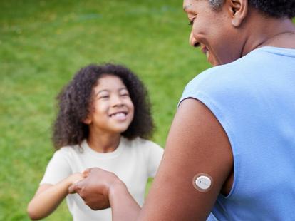 A woman wearing a Dexcom ONE+ on her arm is dancing with a child in the garden