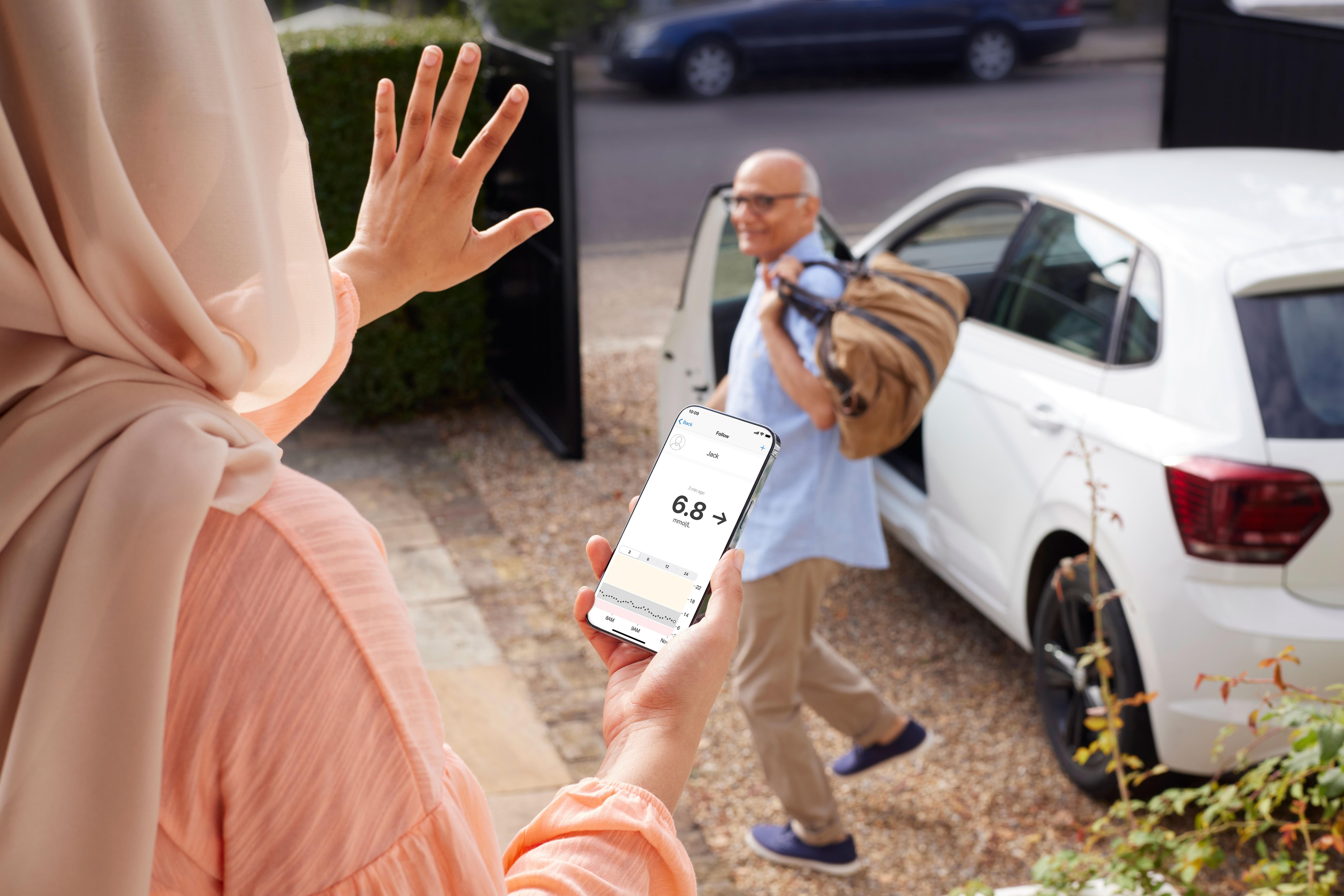A lady holding a smartphone showing the Dexcom app display