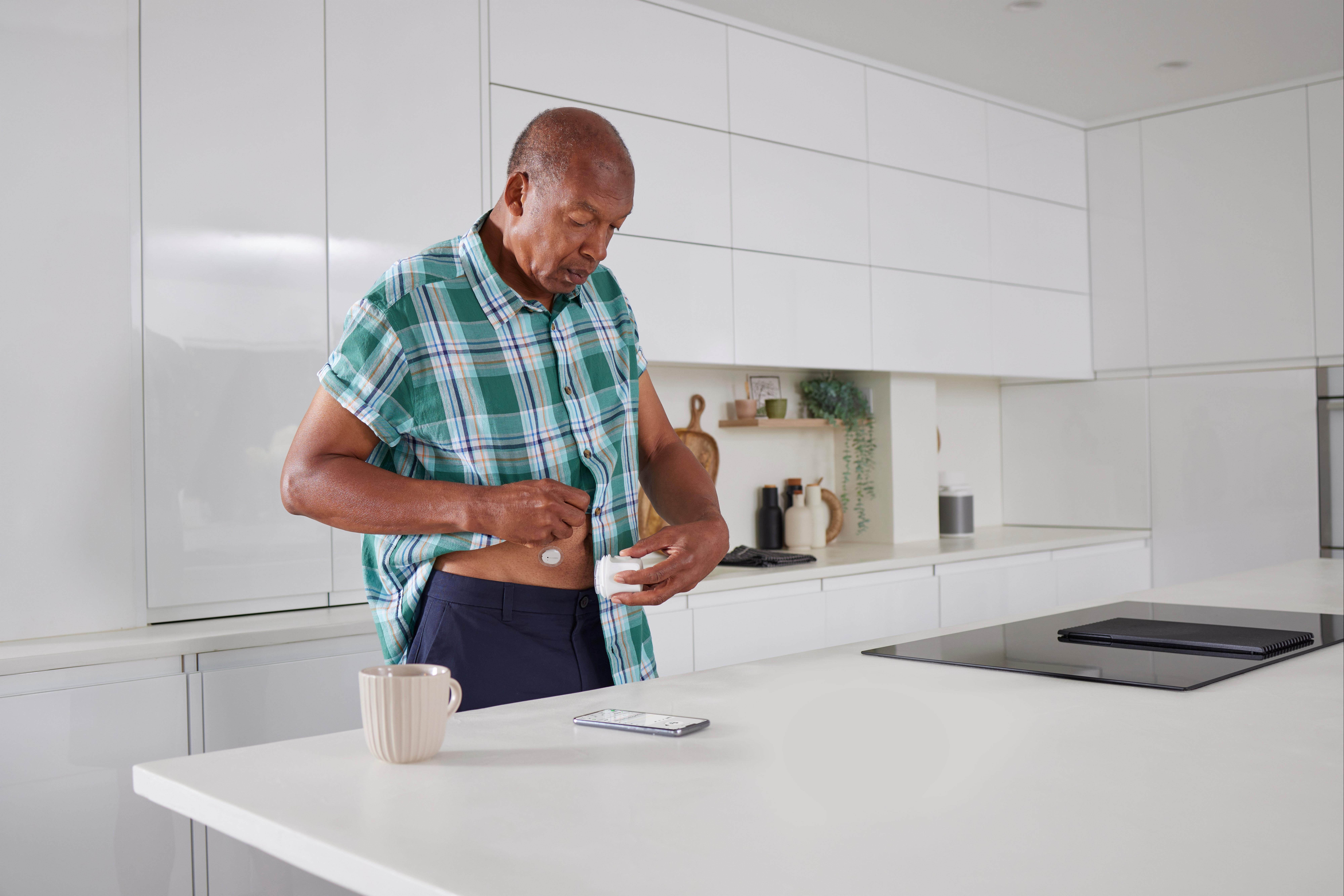 رجل يقف في المطبخ ويضع جهاز استشعار Dexcom ONE+ على بطنه