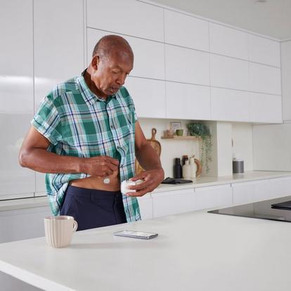 Oudere man in een keuken die een Dexcom ONE+ sensor op zijn buik aanbrengt