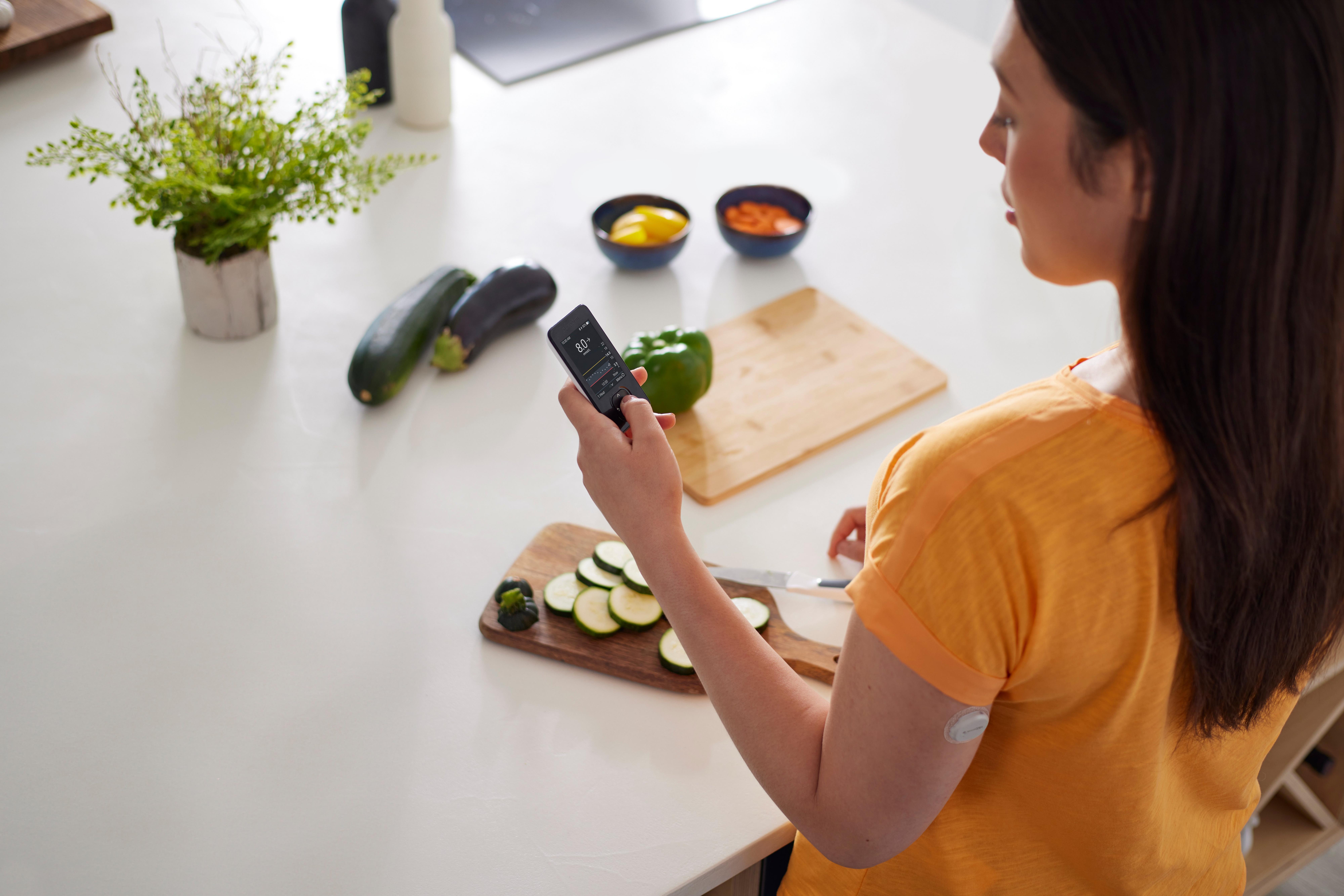 Vrouw met Dexcom ONE+ sensor op haar bovenarm controleert de Dexcom ONE+ ontvanger