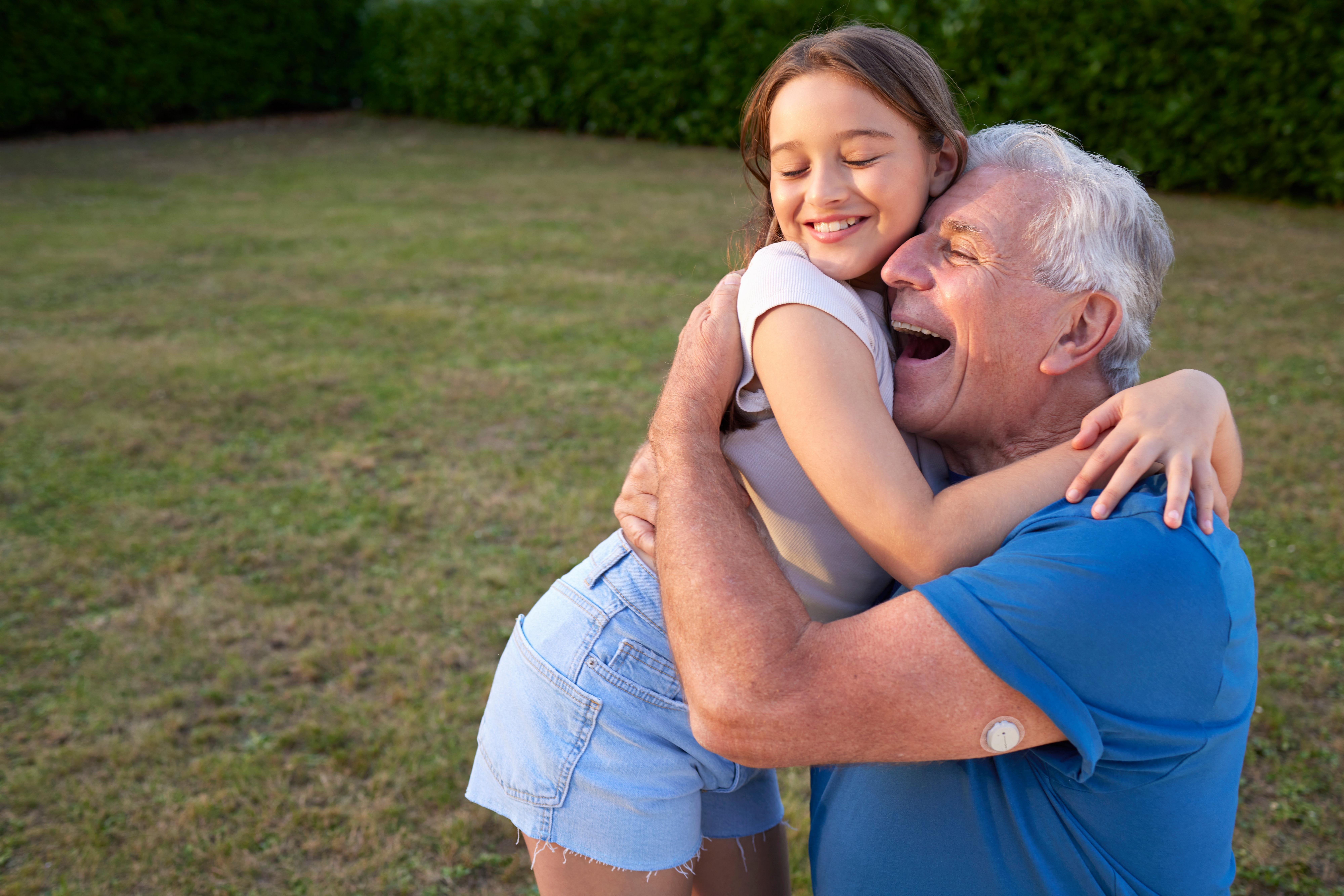 Uomo anziano con sensore Dexcom ONE+ sulla parte superiore del braccio che sorride e abbraccia il nipotino