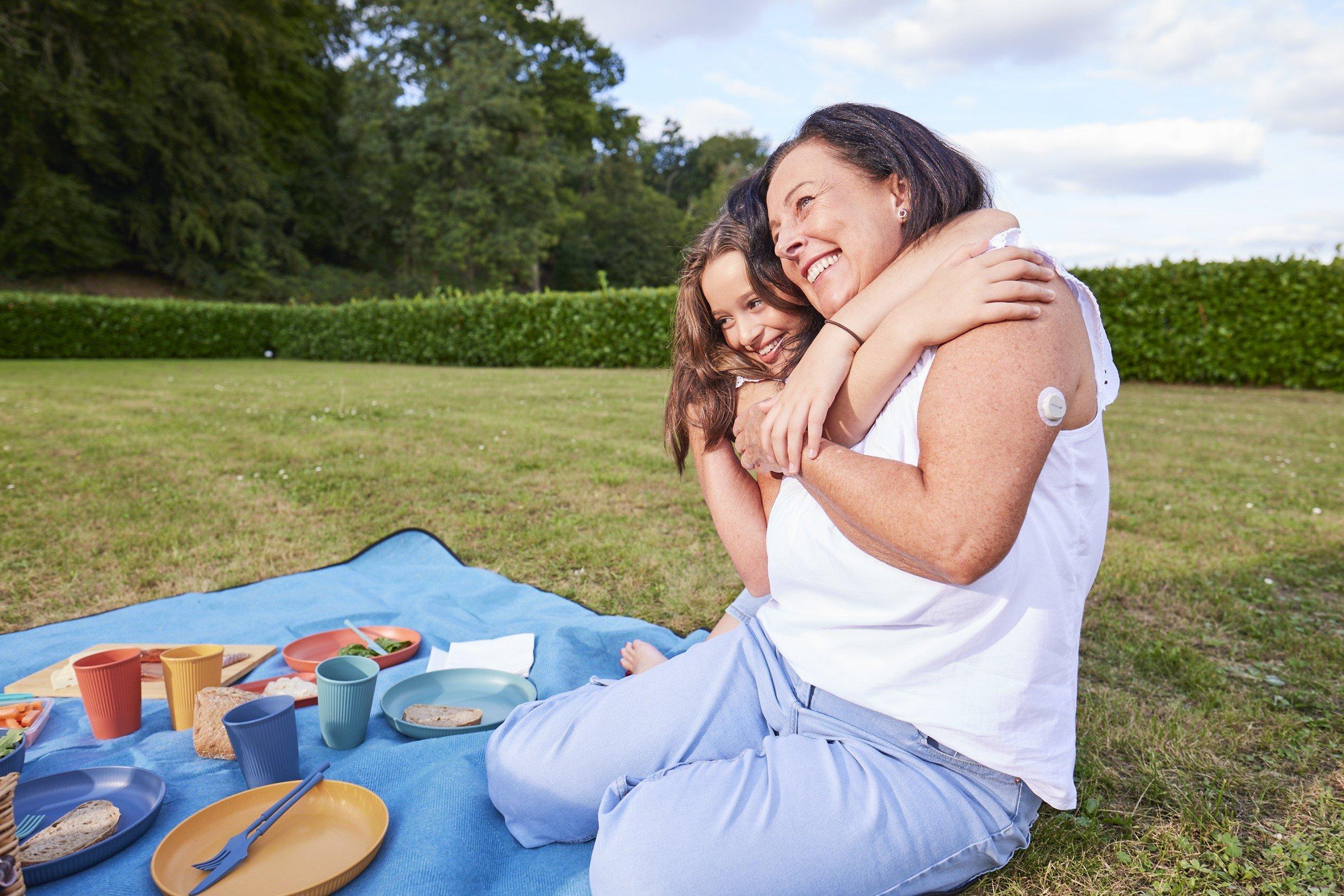 Oudere man met Dexcom ONE+ sensor op zijn bovenarm glimlacht en knuffelt kleinkind