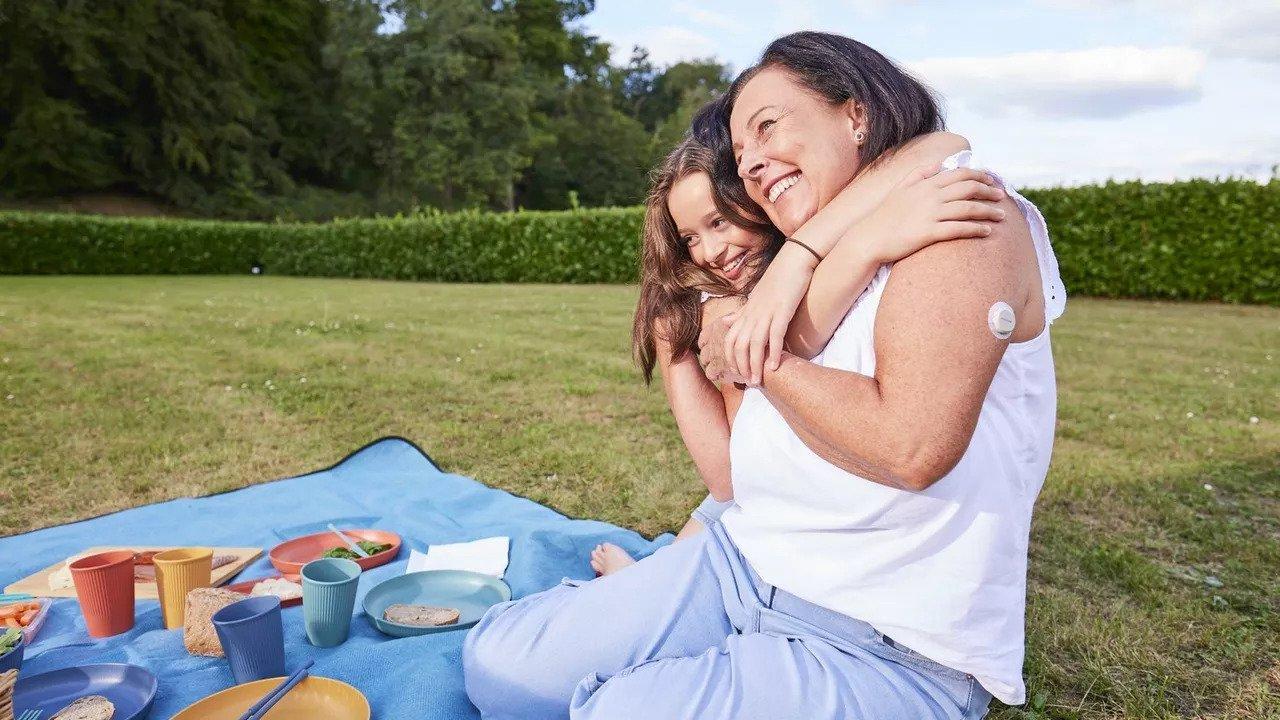 Młoda dziewczyna przytula starszą kobietę z czujnikiem Dexcom ONE+ na ramieniu