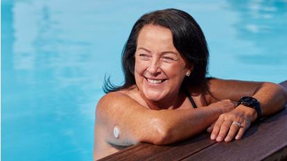 Vrouw aan de rand van zwembad met Dexcom ONE+ sensor op haar bovenarm