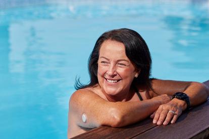 Kvinna vid sidan av poolen med Dexcom ONE+ sensor på överarmen