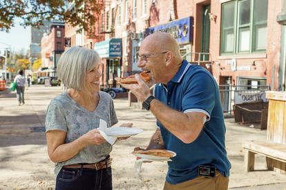 Couple âgé dehors au soleil, mangeant une pizza et riant