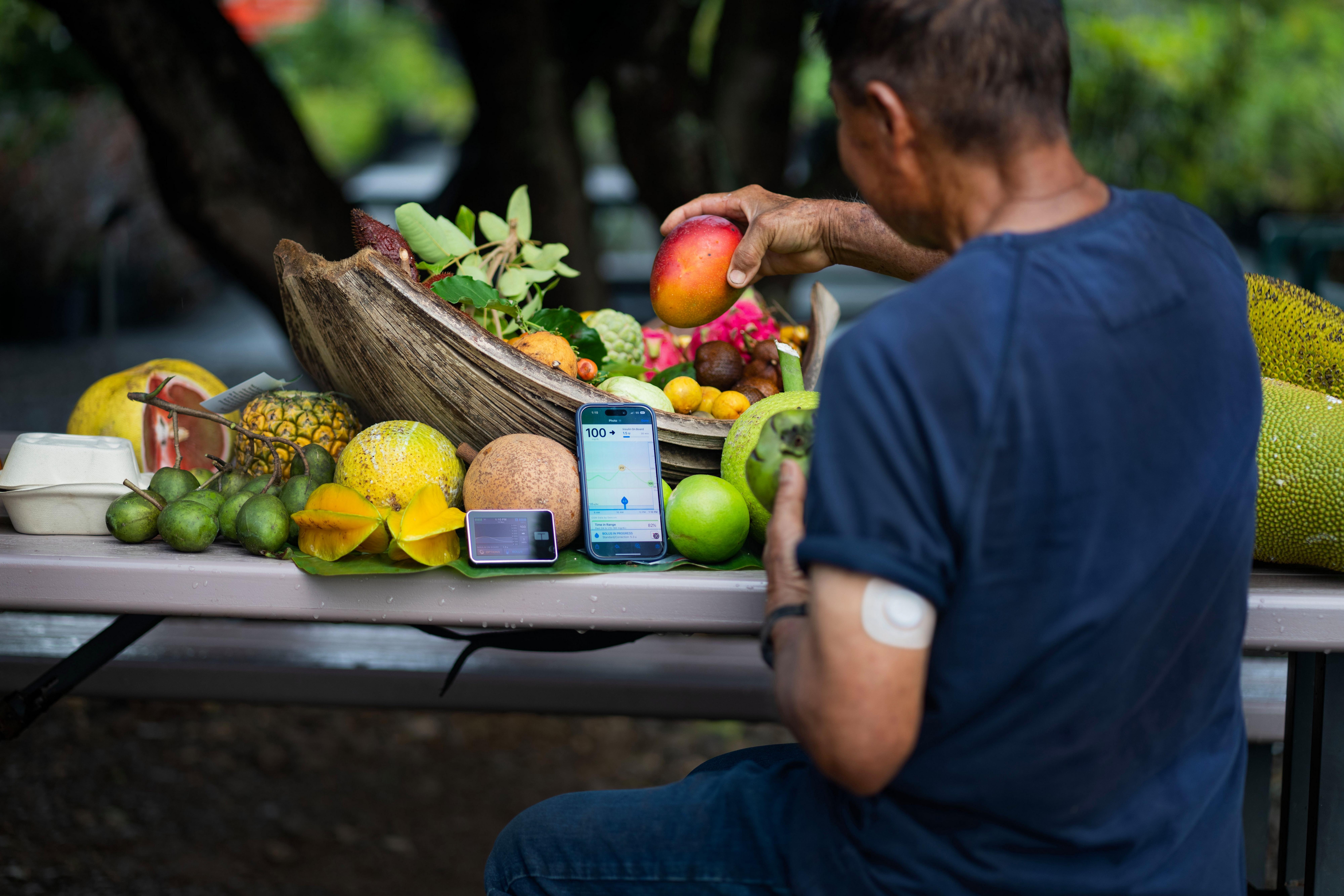 Man putting fruits in a basket while wearing a Dexcom sensor and watching glucose levels on the app