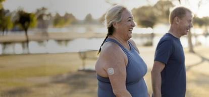 Woman walking outside with friend and wearing a Dexcom G7 CGM sensor on back of her arm.