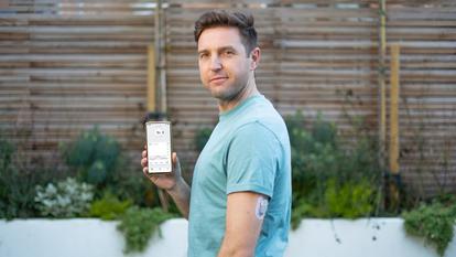 Vyras, vilkintis marškinėlius su "dexcom Continous" gliukozės stebėsenos prietaisu ant nugaros ir laikantis išmanųjį telefoną