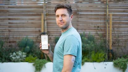 Άνδρας που κρατά ψηλά το τηλέφωνο με την εφαρμογή Dexcom και τις τιμές γλυκόζης - Μικρογραφία βίντεο