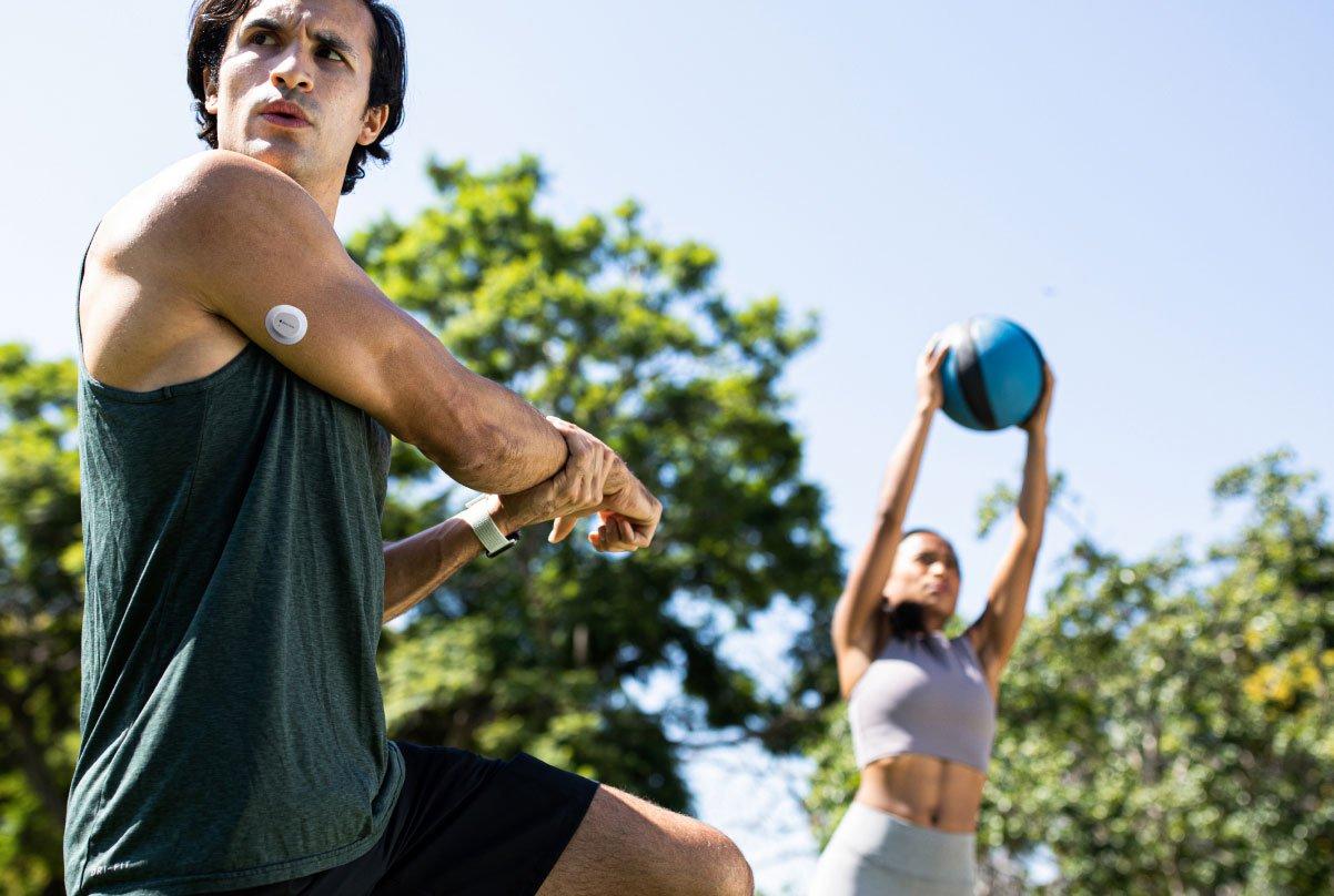Hombre al aire libre estirando el brazo con un sensor Dexcom en la parte superior del brazo.