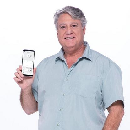 Vyras su pilkais marškiniais, laikantis mobilųjį telefoną