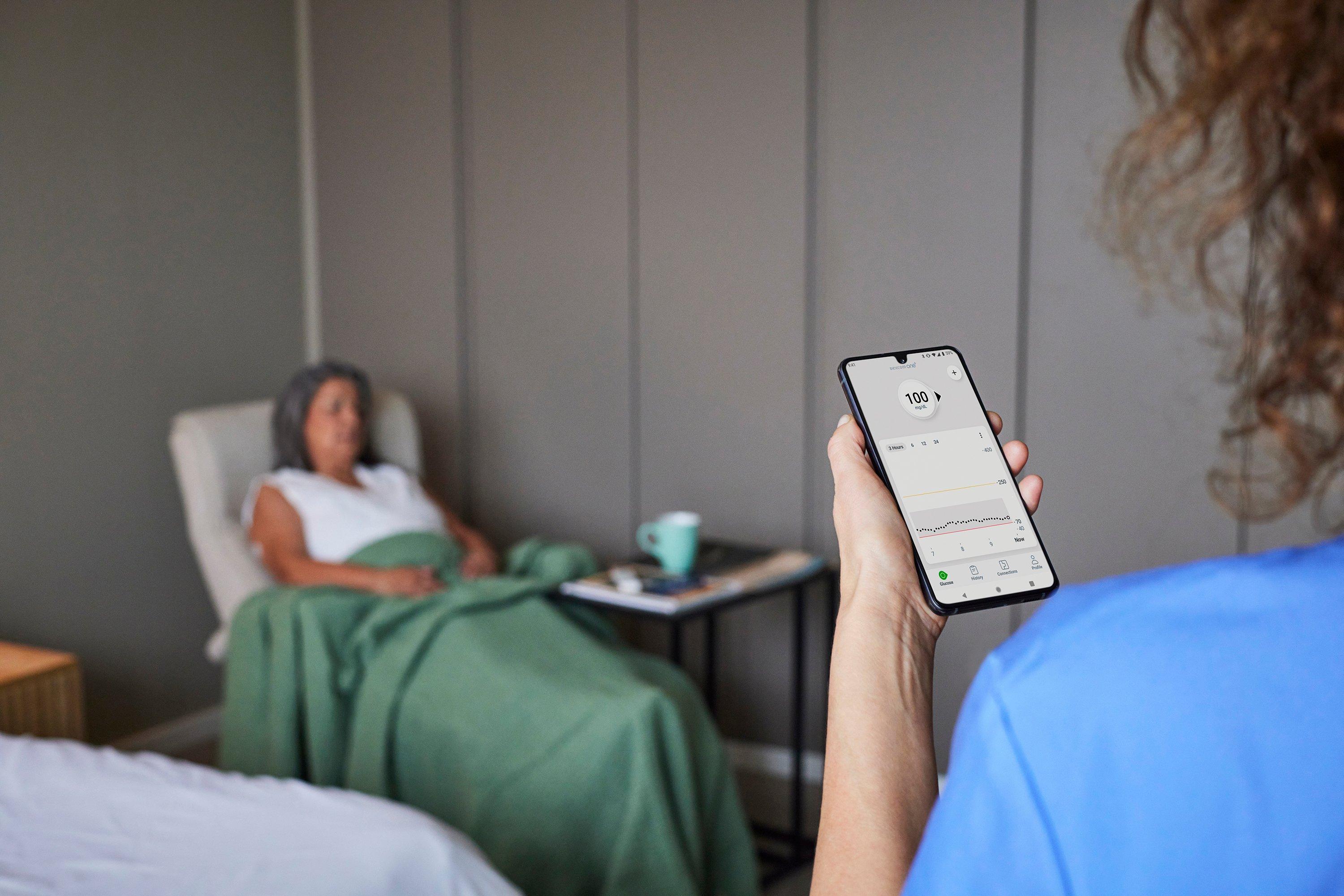 ممرضة في المستشفى تقرأ قيم الجلوكوز على تطبيق Dexcom على الهاتف