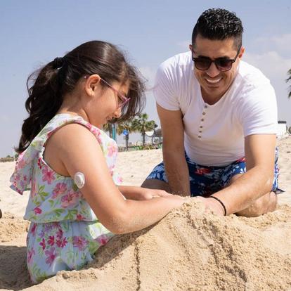 Father playing with daughter with D1+ device on her arm in the sand