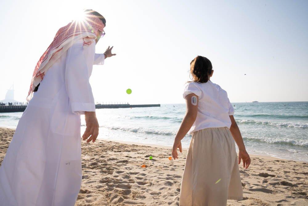 Man and girl with Dexcom device on her arm playing with balls at the beach