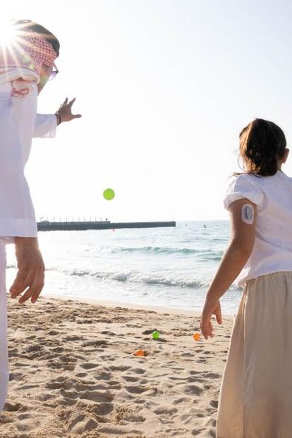 Man and girl with Dexcom device on her arm playing with balls at the beach