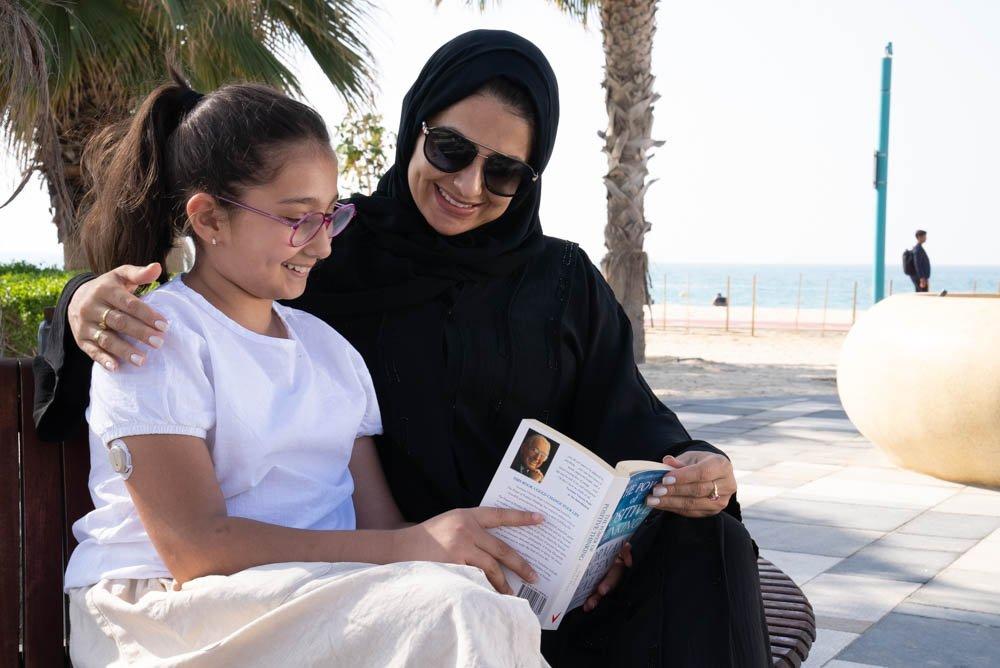 امرأة وابنتها تجلسان على المقعد وتقرأان كتابًا