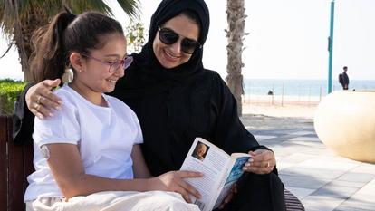 Woman and daughter sitting on bench reading a book