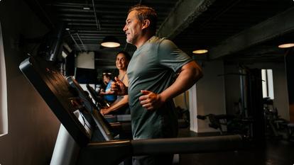 Man running on a treadmill woman smiling beside him