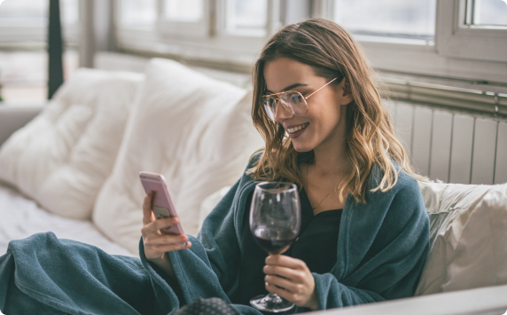 woman drinking red wine looking at phone on couch