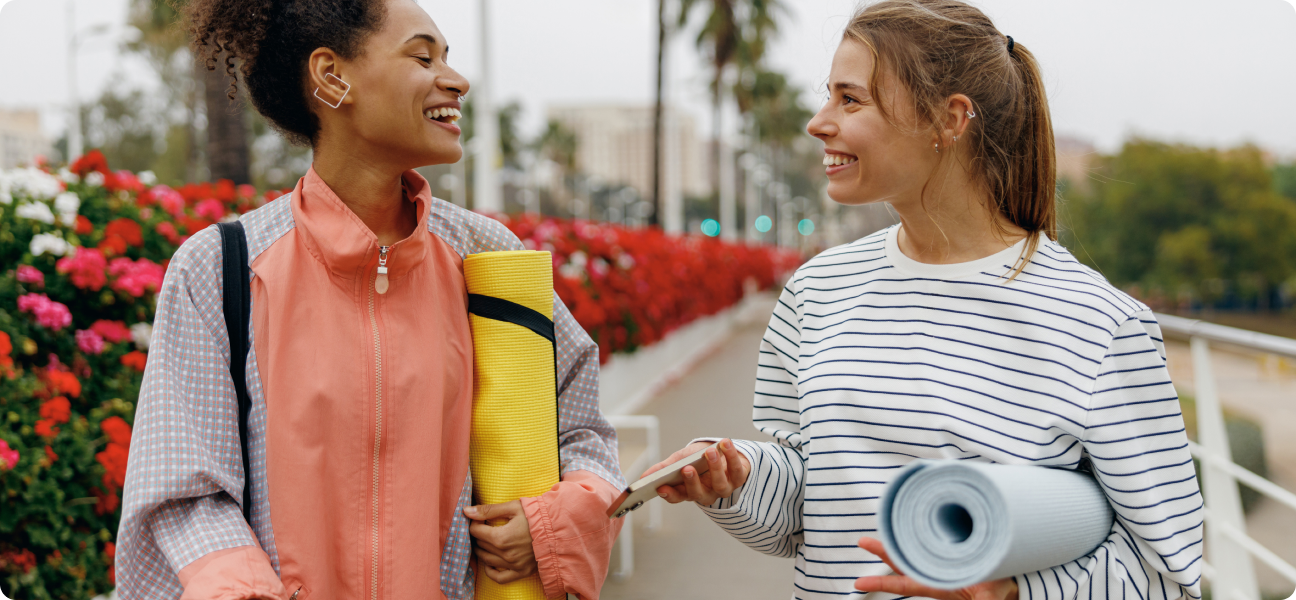Two women outside holding yoga mats