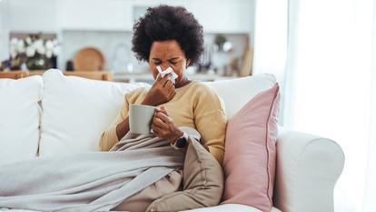Sick woman sitting on couch blowing nose