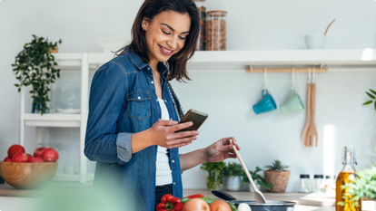 Woman in kitchen cooking and looking at phone