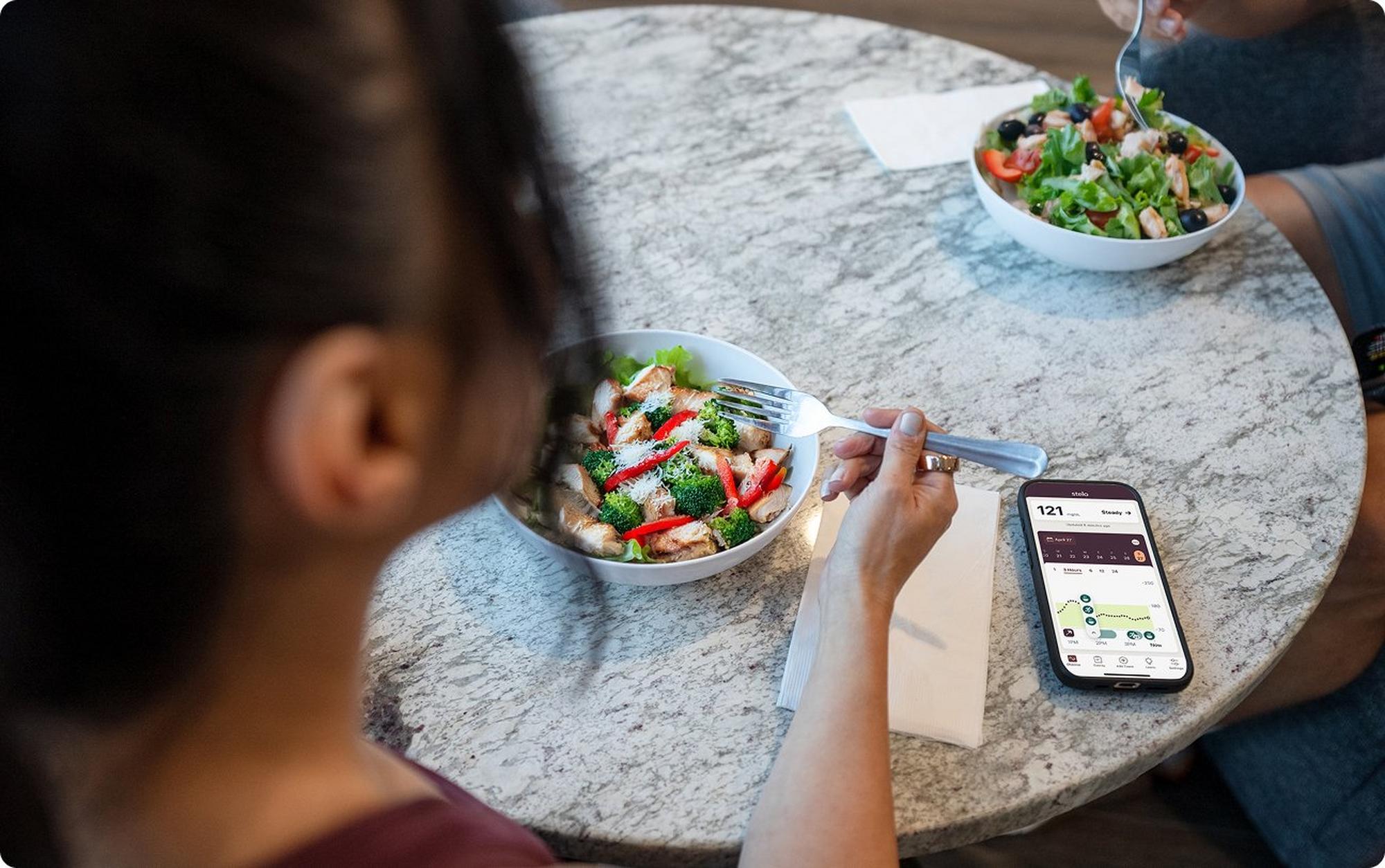 woman eating lunch looking at stelo app on smart device