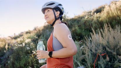 woman wearing bike helmet and stelo biosensor holding bottle of water