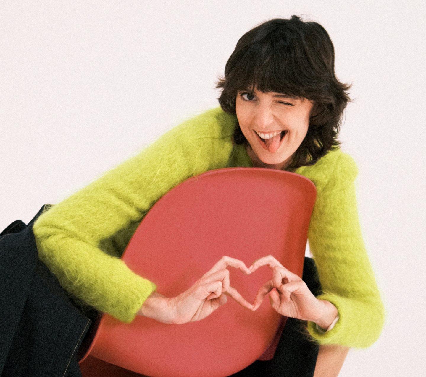 glucose goddess sitting in chair with finger hearts