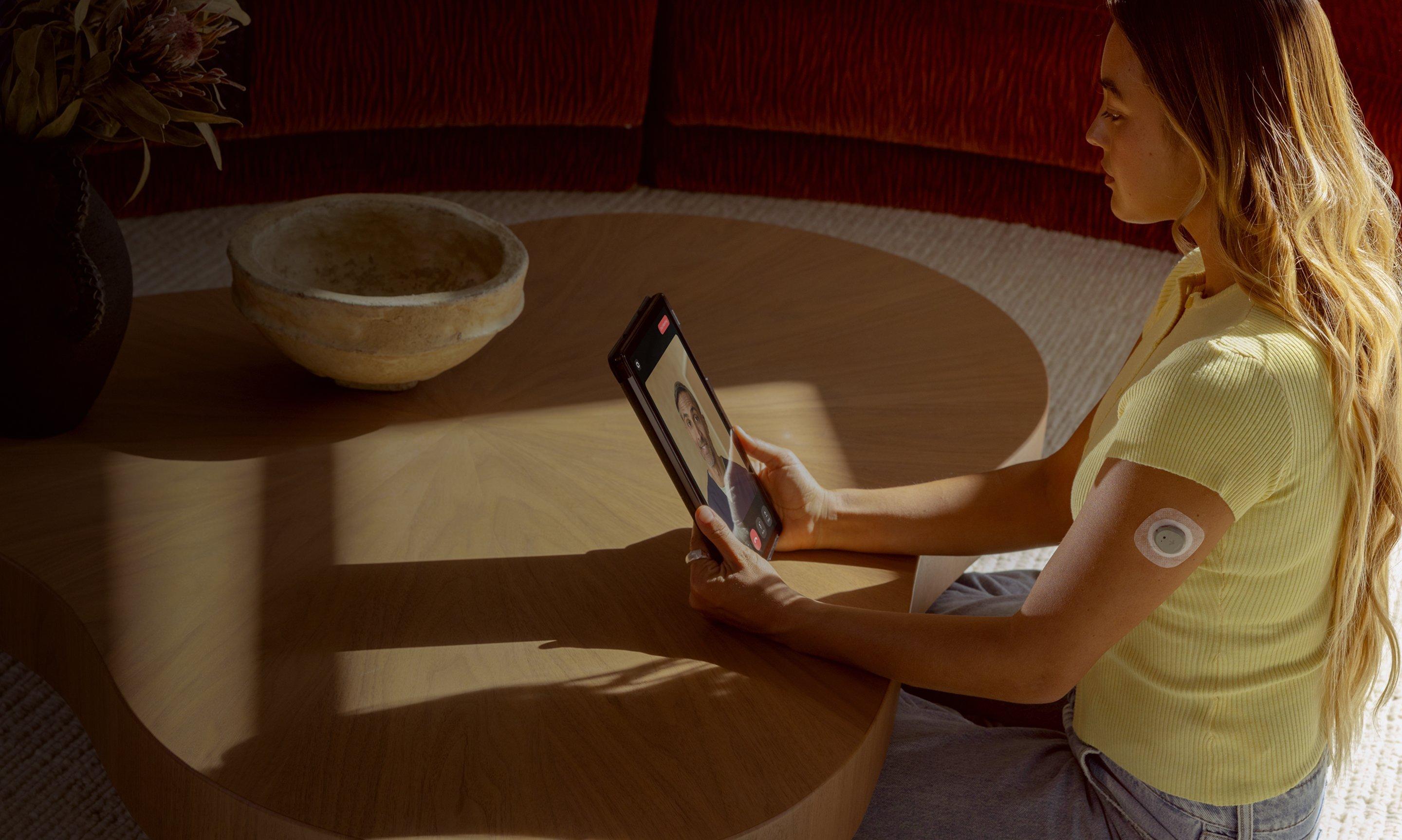 Woman wearing Stelo glucose biosensor on her arm and attending a video call with a nutritionist.