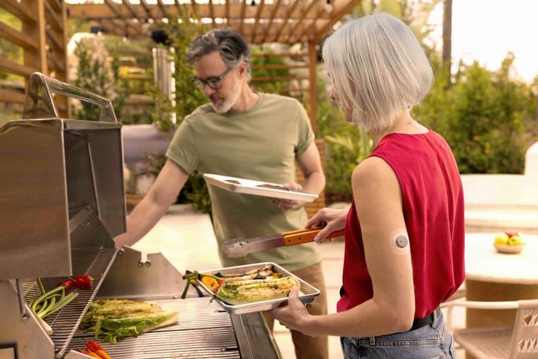 A man and a woman cooking food outdoors on a grill