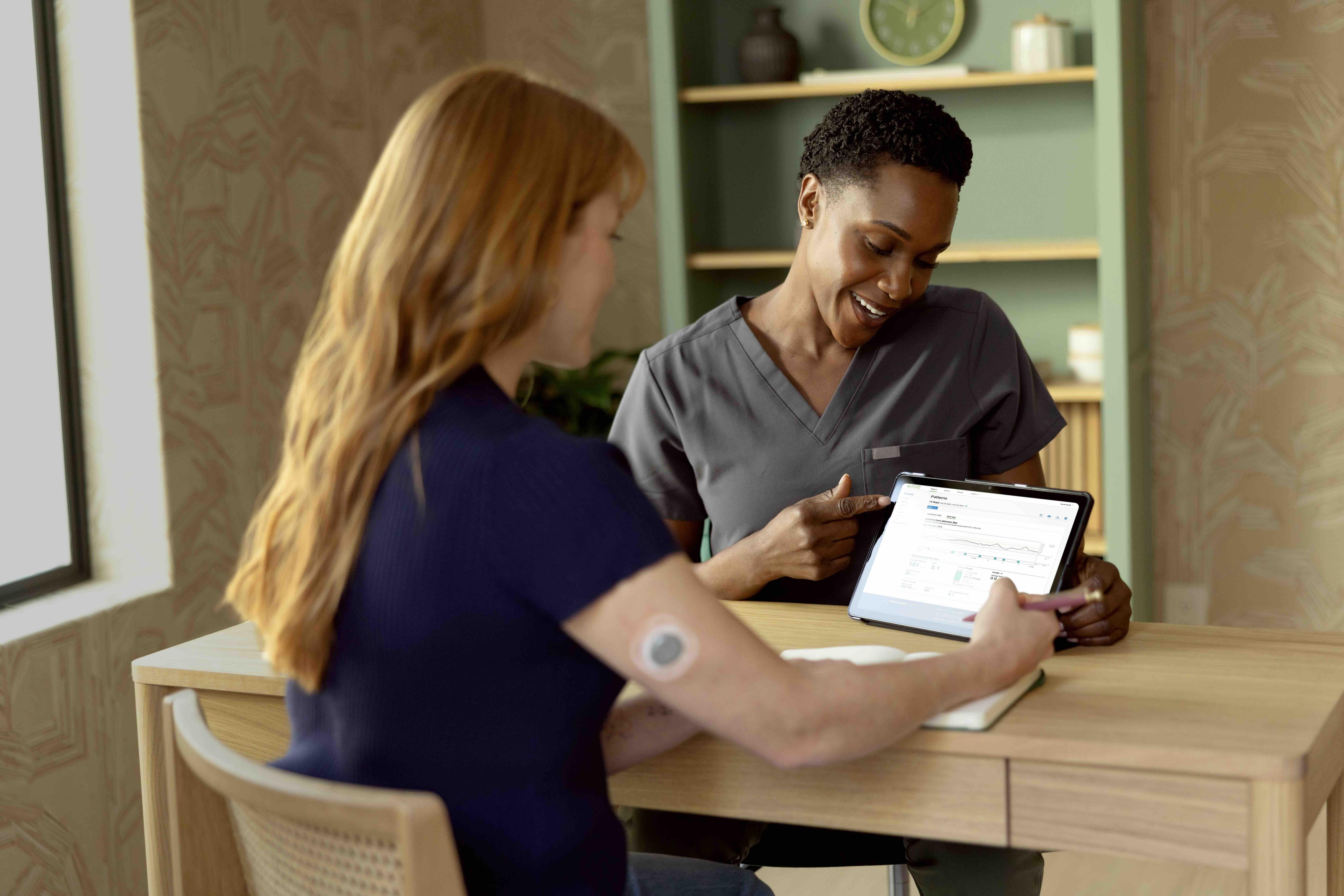 Female provider sitting down with a female patient, reviewing patient information on tablet.